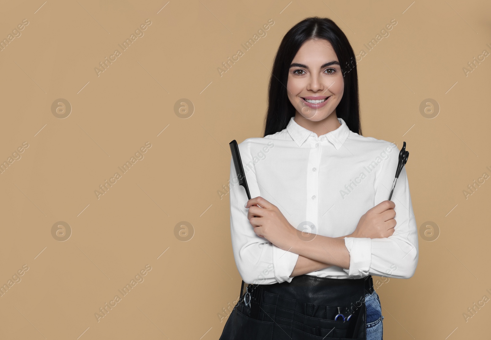 Photo of Portrait of happy hairdresser with professional scissors and comb on beige background, space for text