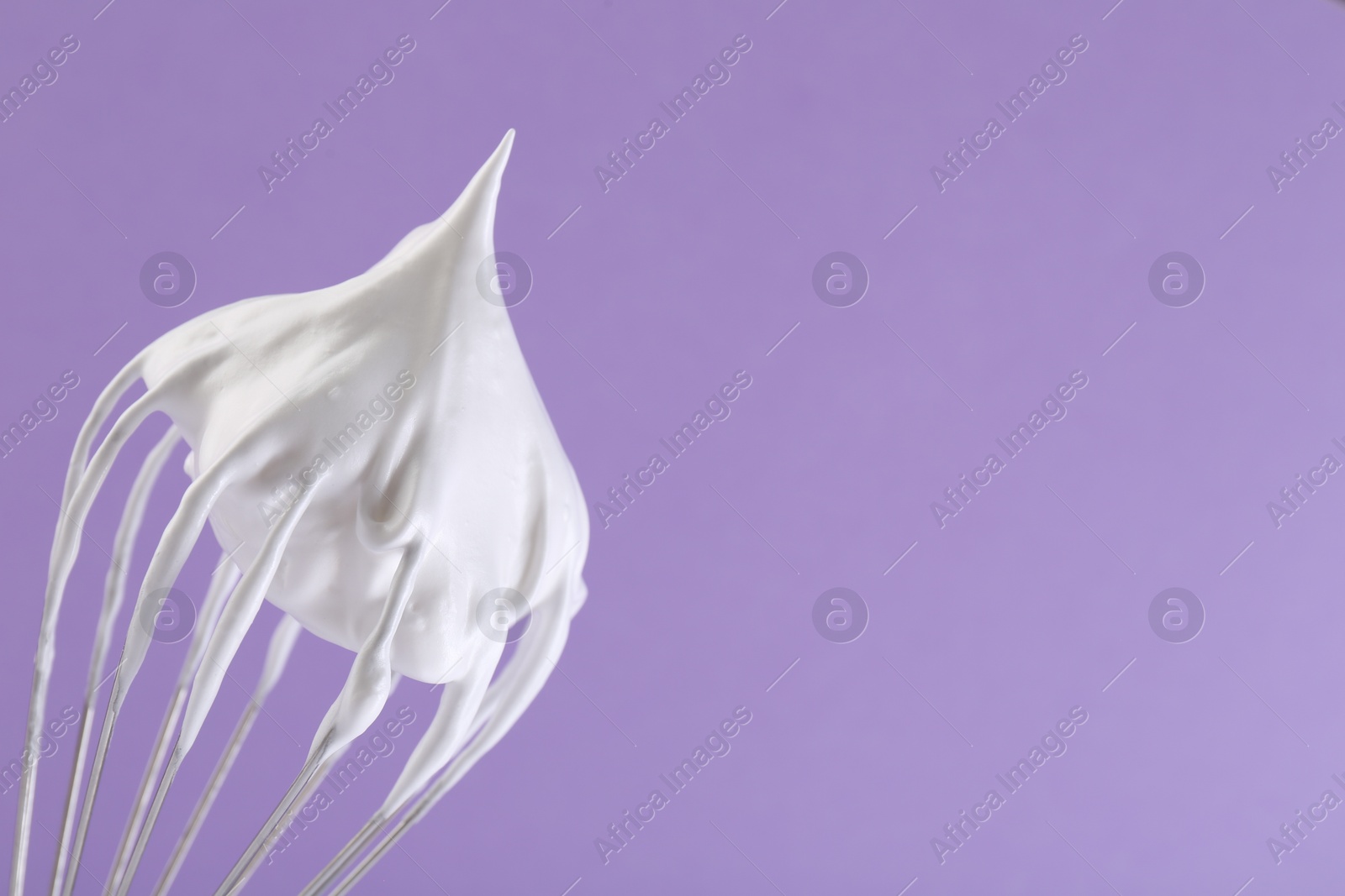 Photo of Whisk with whipped cream on violet background, closeup. Space for text