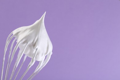Photo of Whisk with whipped cream on violet background, closeup. Space for text