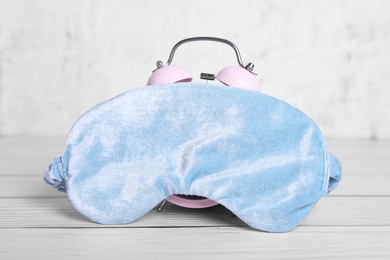 Photo of Soft sleep mask and alarm clock on white wooden table, closeup