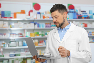 Image of Professional pharmacist with laptop in modern drugstore