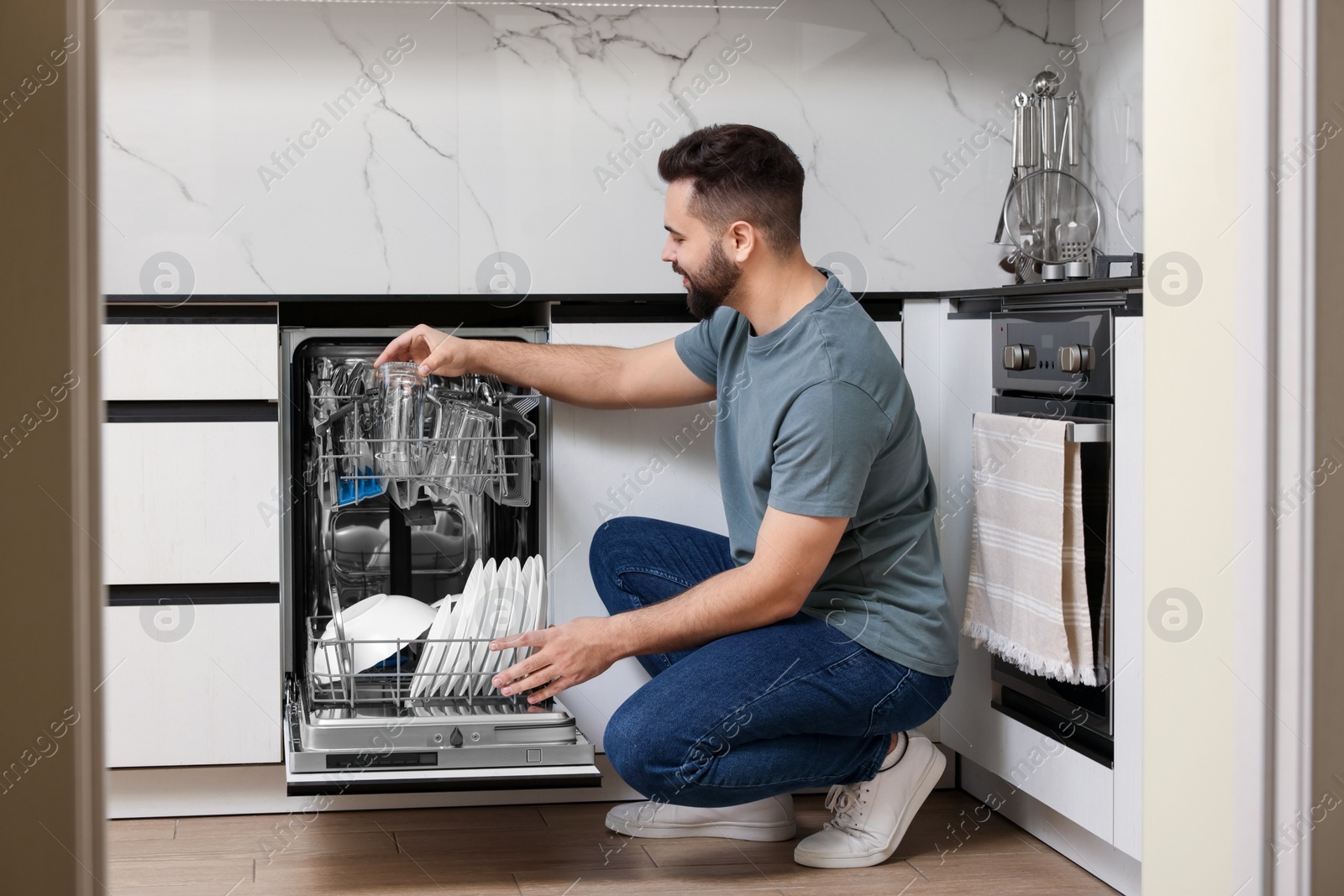 Photo of Man loading dishwasher with glasses in kitchen
