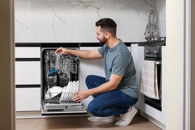 Man loading dishwasher with glasses in kitchen