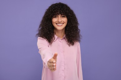 Photo of Happy young woman welcoming and offering handshake on violet background