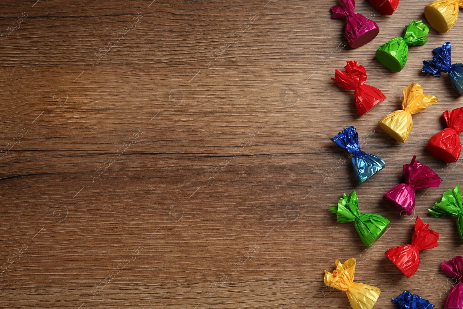 Photo of Many candies in colorful wrappers on wooden table, flat lay. Space for text