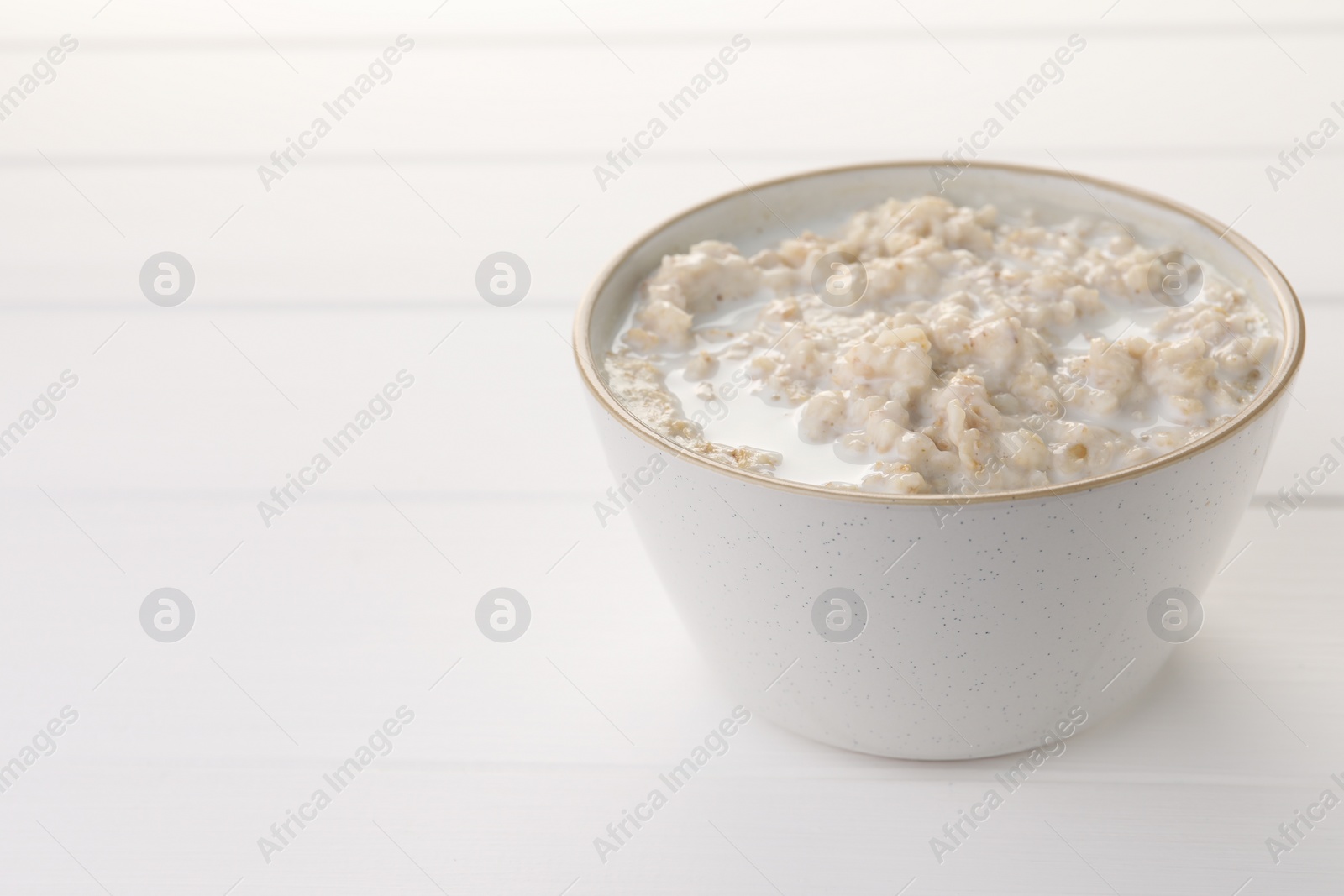 Photo of Tasty boiled oatmeal in bowl on white wooden table, closeup. Space for text