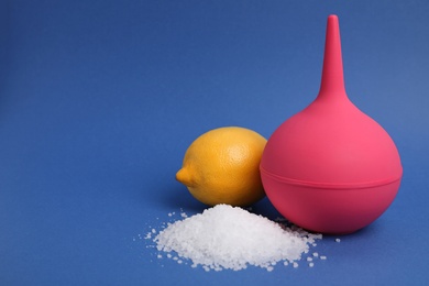 Photo of Enema, lemon and heap of salt on blue background, space for text. Medical treatment