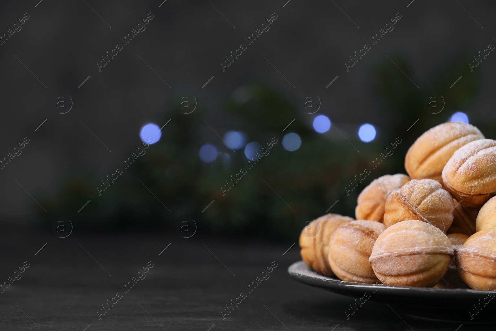 Photo of Plate of tasty nut shaped cookies with powdered sugar on black table, closeup. Space for text