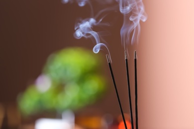 Photo of Incense sticks smoldering on blurred background, closeup. Space for text