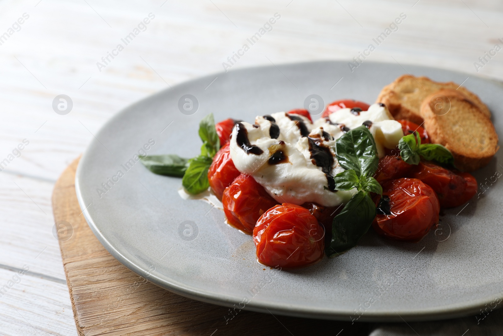Photo of Delicious burrata cheese served with tomatoes, croutons and basil sauce on white wooden table, closeup