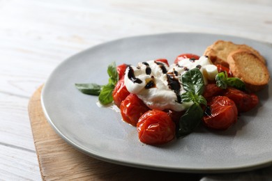 Delicious burrata cheese served with tomatoes, croutons and basil sauce on white wooden table, closeup