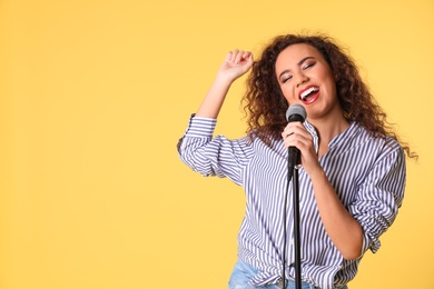 Portrait of curly African-American woman singing in microphone on color background. Space for text