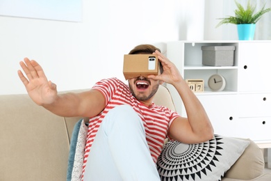 Photo of Young man using cardboard virtual reality headset at home