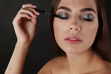 Photo of Portrait of beautiful woman applying stylish makeup with brush on dark background
