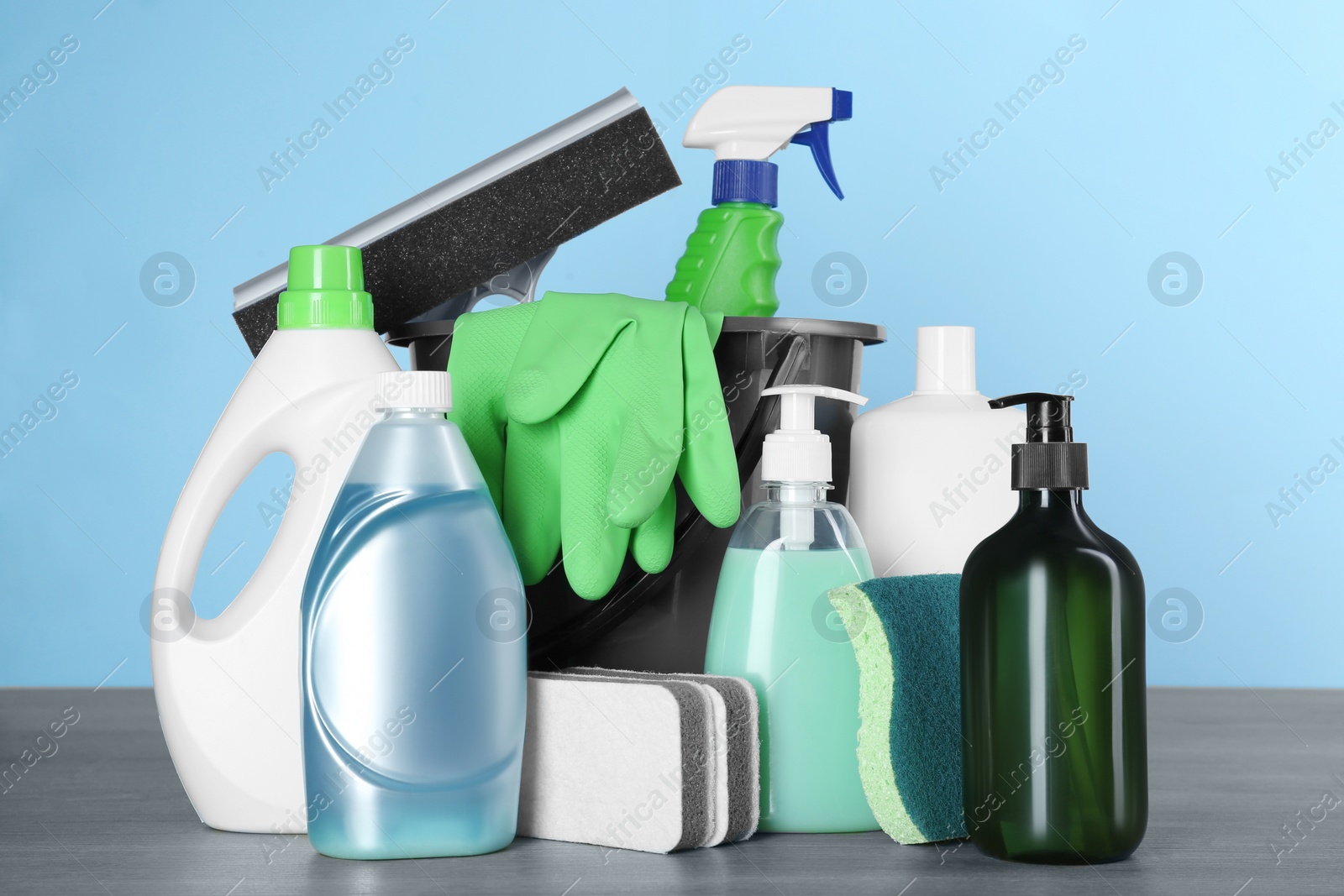 Photo of Different cleaning supplies and tools on wooden table against light blue background