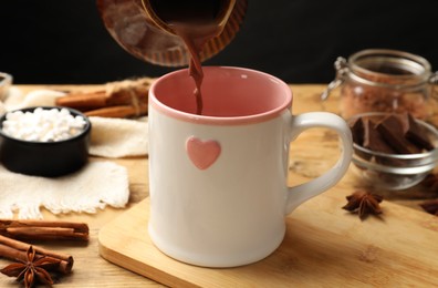 Photo of Pouring tasty hot chocolate into cup at wooden table, closeup