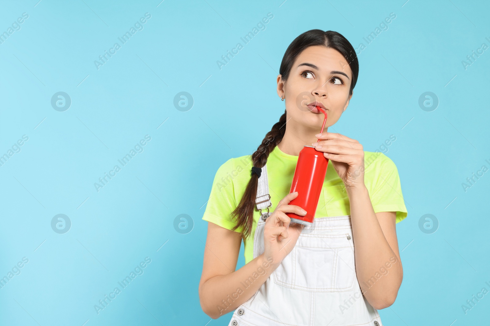 Photo of Beautiful happy woman drinking from red beverage can on light blue background. Space for text