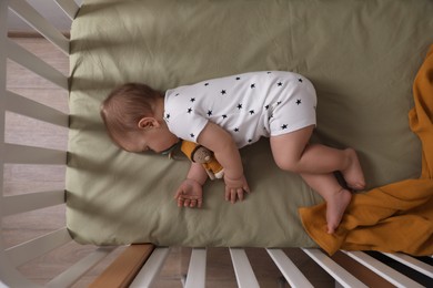 Adorable little baby with pacifier sleeping in crib indoors, top view