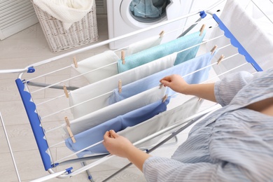 Photo of Woman hanging clean laundry on drying rack indoors, closeup