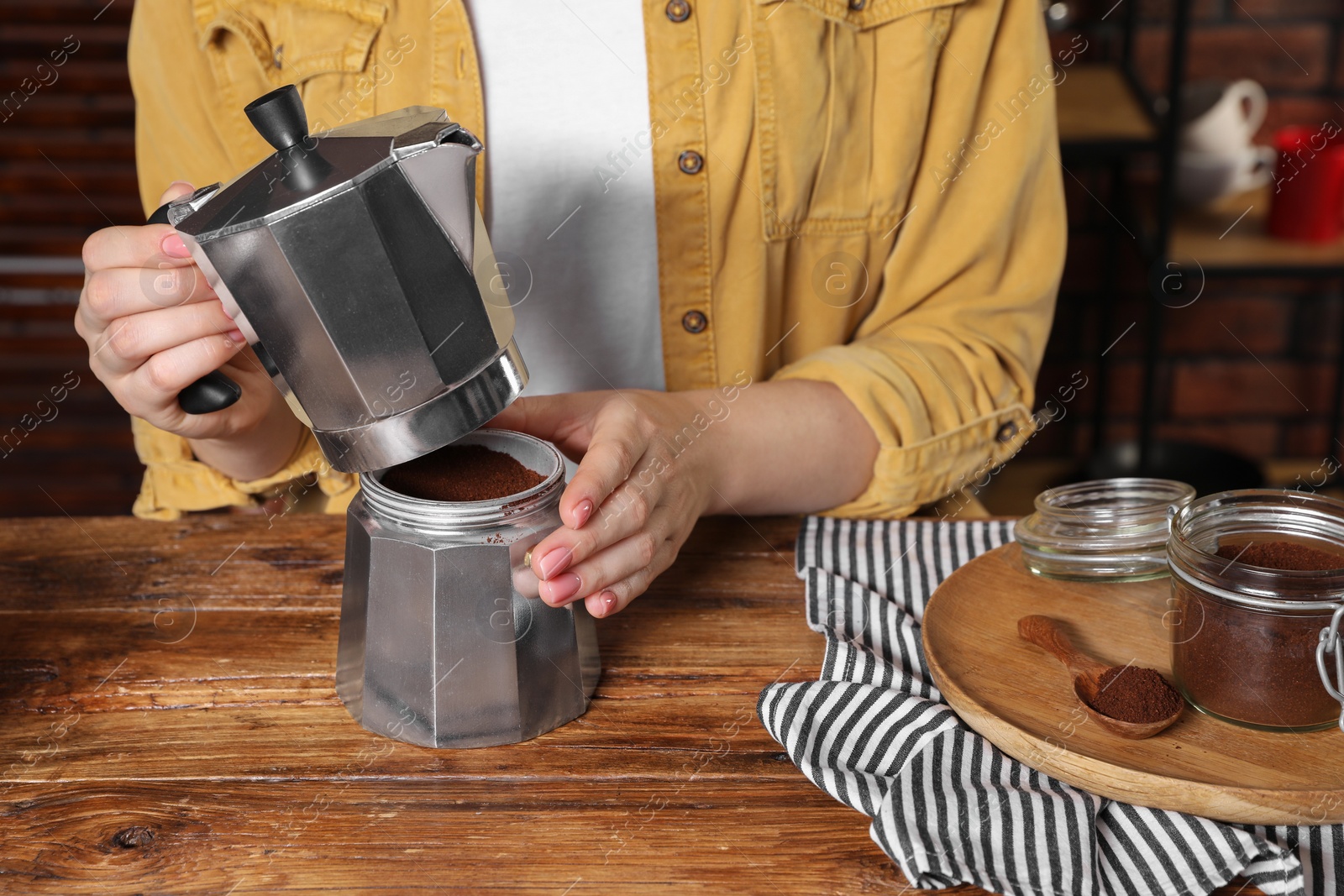 Photo of Woman making coffee in moka pot at wooden table, closeup