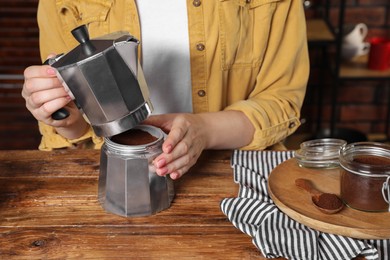 Woman making coffee in moka pot at wooden table, closeup