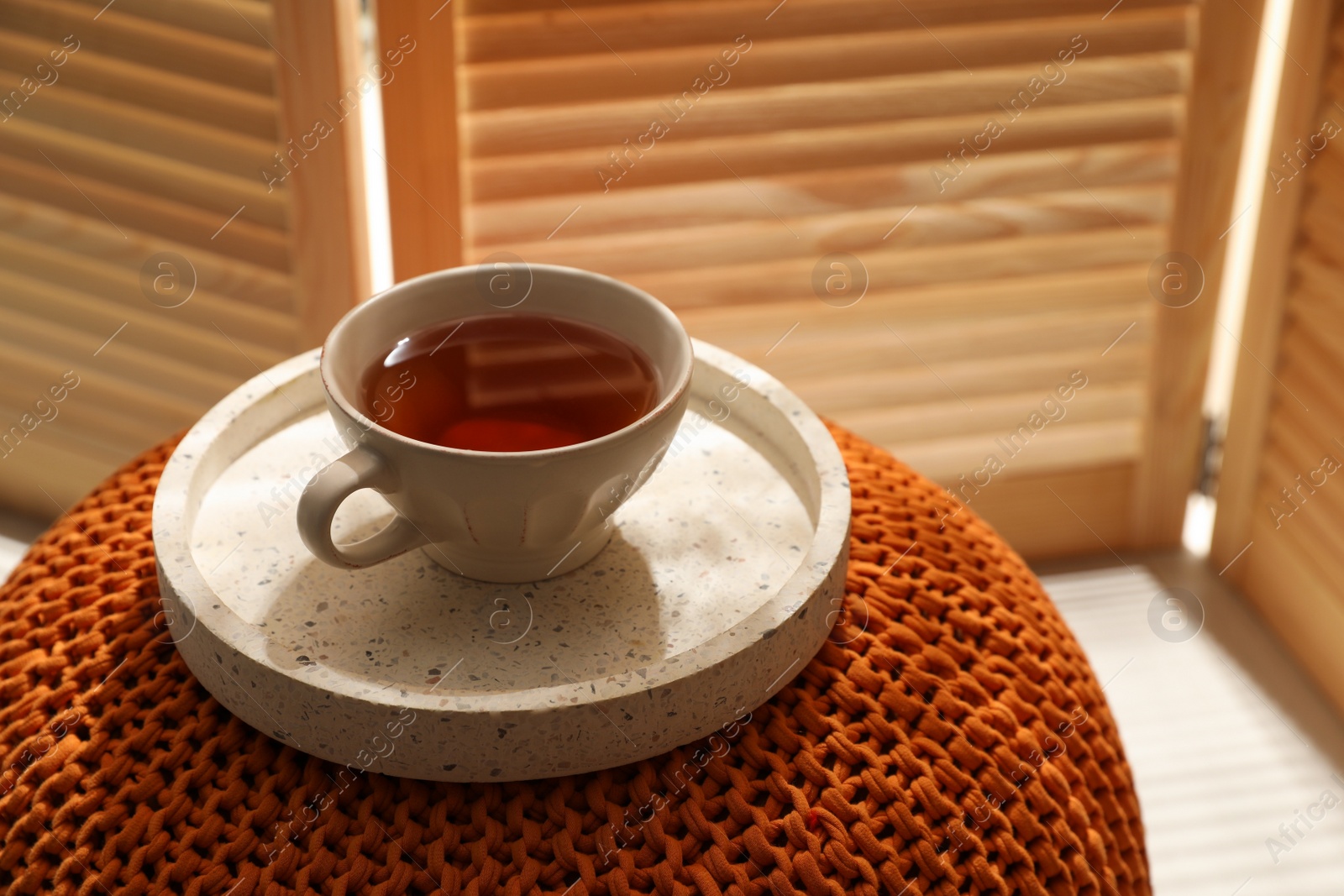 Photo of Tray with cup of tea on comfortable pouf in room, space for text