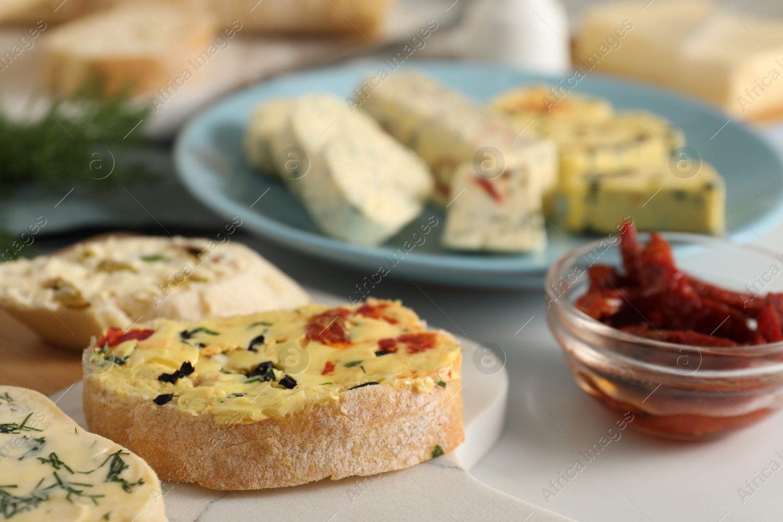 Photo of Different types of tasty butter, chili peppers and bread on white table, closeup