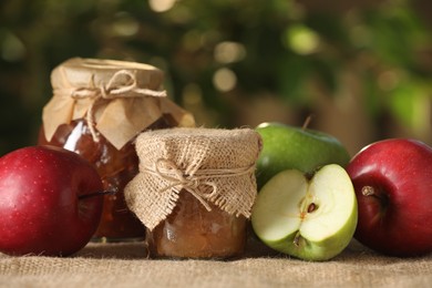 Photo of Delicious apple jam and fresh fruits on burlap against blurred background, closeup