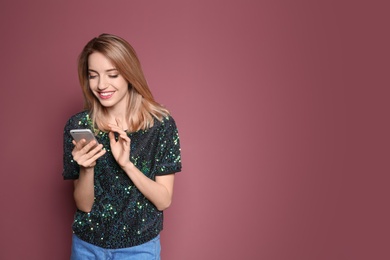 Young woman using phone on color background