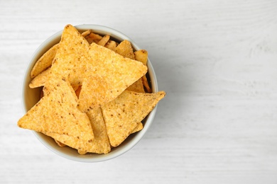 Bowl with tasty Mexican nachos chips on white wooden table, top view. Space for text