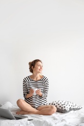 Female blogger with laptop and cup of coffee on bed