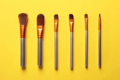 Photo of Different makeup brushes on yellow background, flat lay