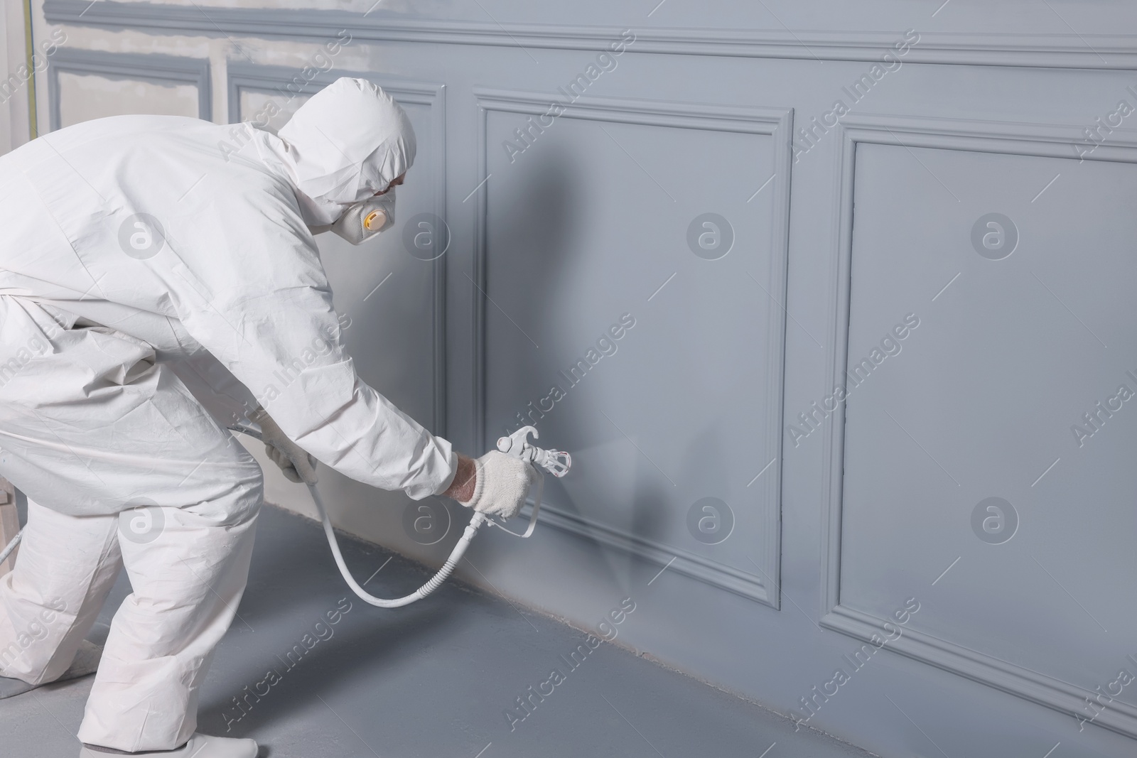 Photo of Decorator dyeing wall in grey color with spray paint indoors, space for text