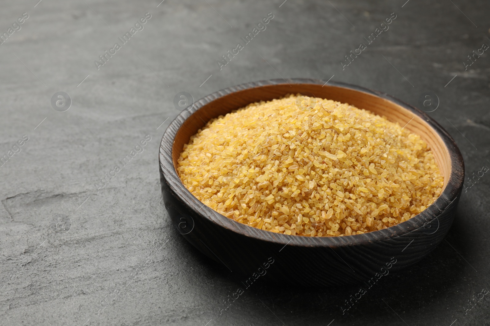 Photo of Raw bulgur in bowl on dark gray table, closeup