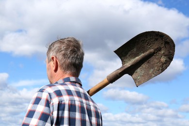 Man holding shovel against cloudy sky, back view. Digging process
