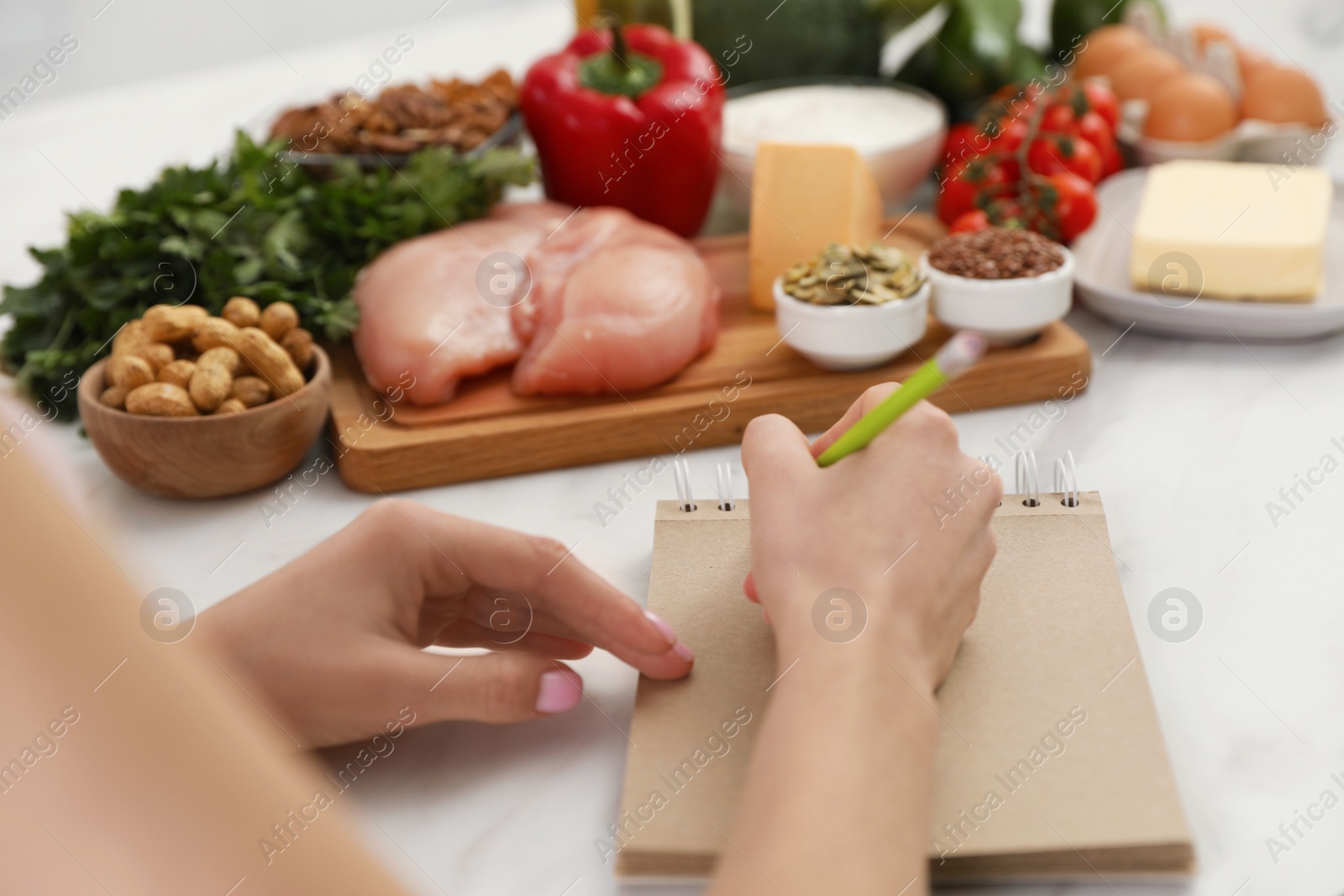 Photo of Woman writing in notebook near products at table, closeup. Keto diet