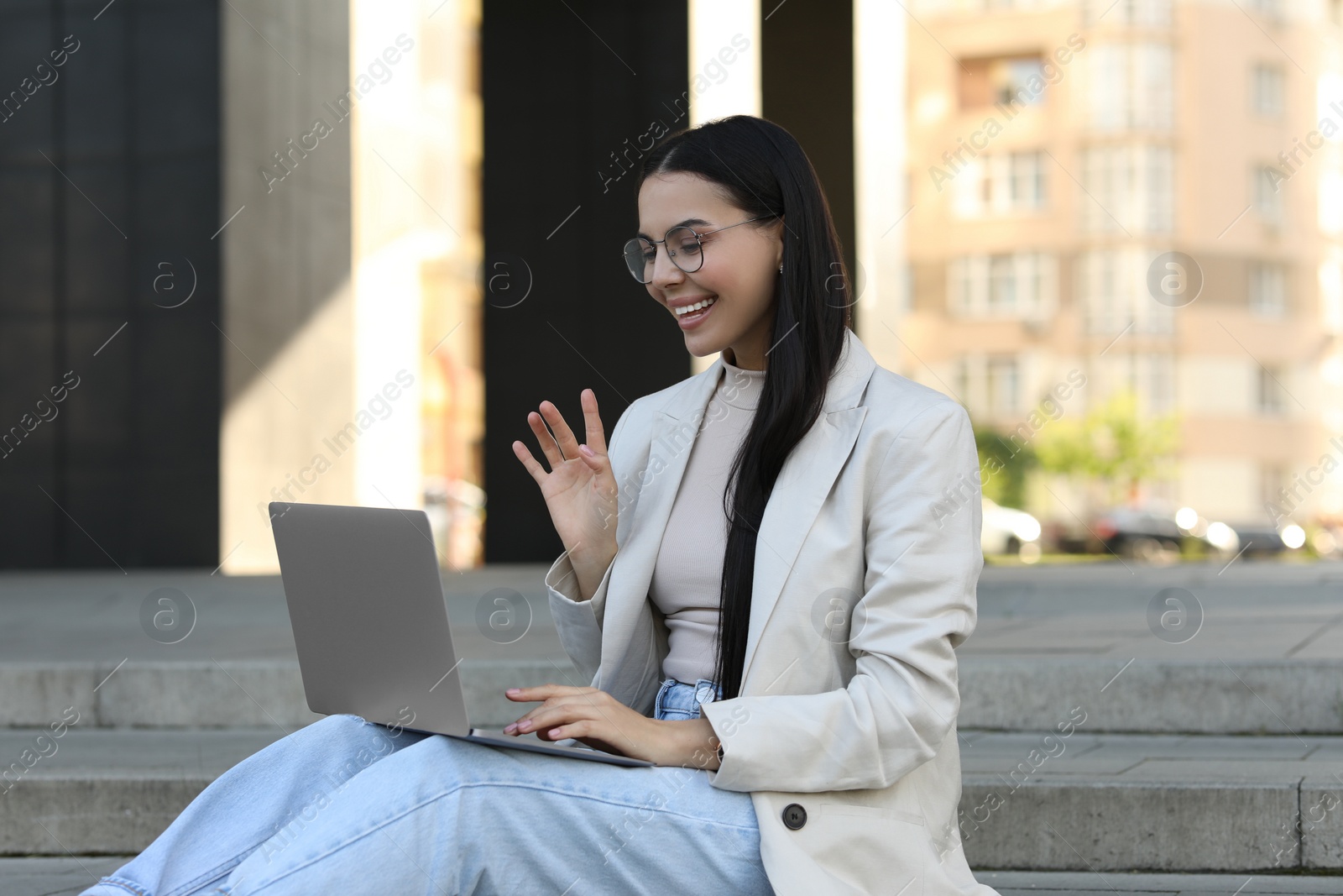 Photo of Happy young woman using modern laptop for video call outdoors