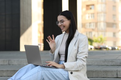 Photo of Happy young woman using modern laptop for video call outdoors