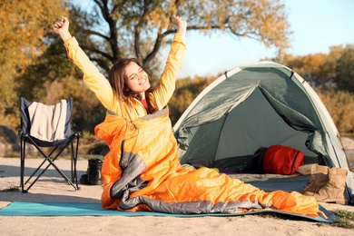 Young woman stretching in sleeping bag near camping tent outdoors