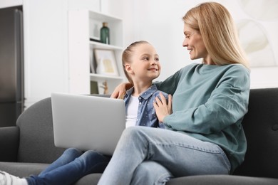 Happy woman and her daughter with laptop on sofa at home