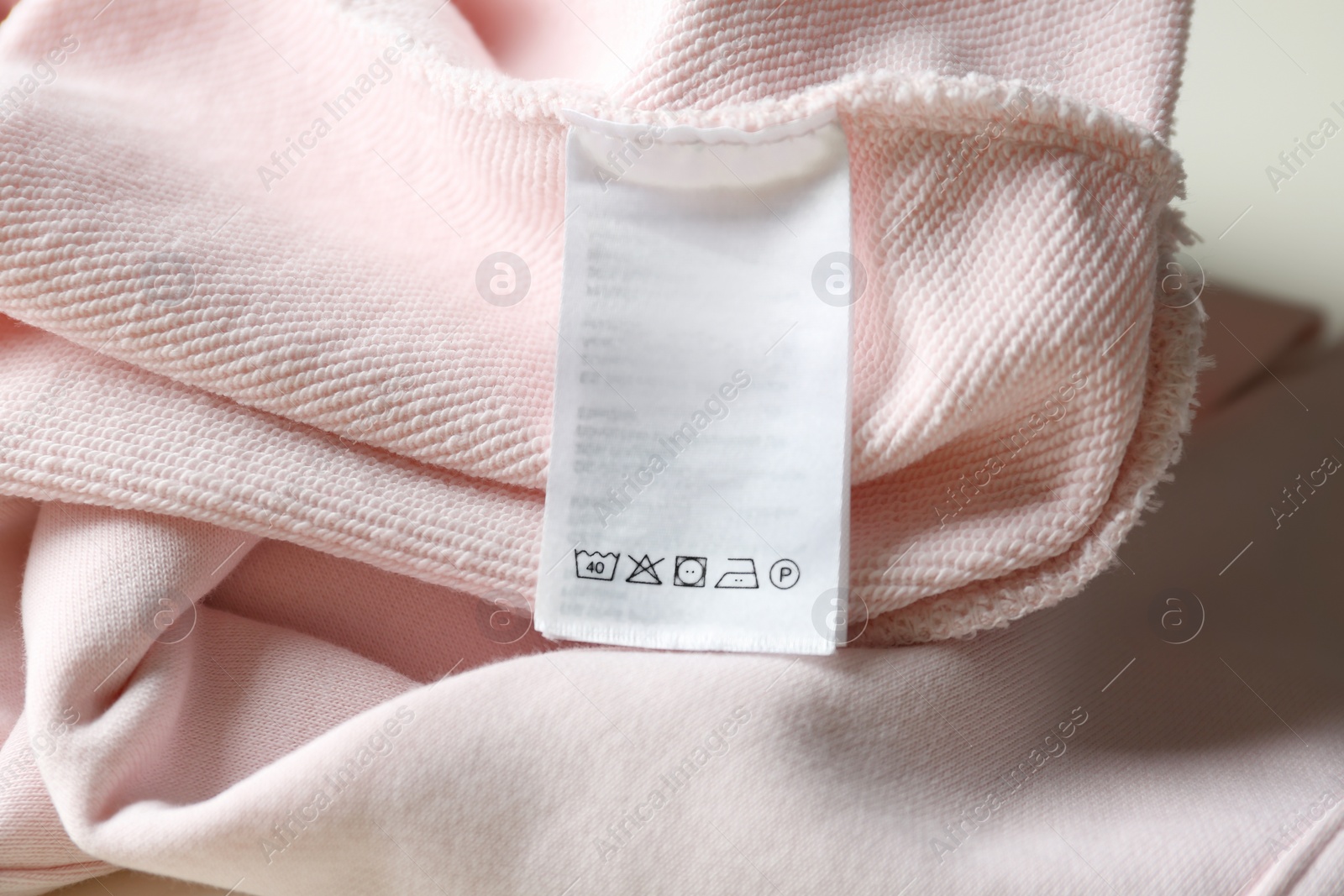 Photo of Clothing label with care instructions on pink garment, closeup
