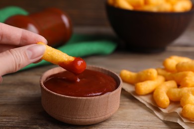 Photo of Woman dipping tasty cheesy corn stick in red sauce at wooden table, closeup