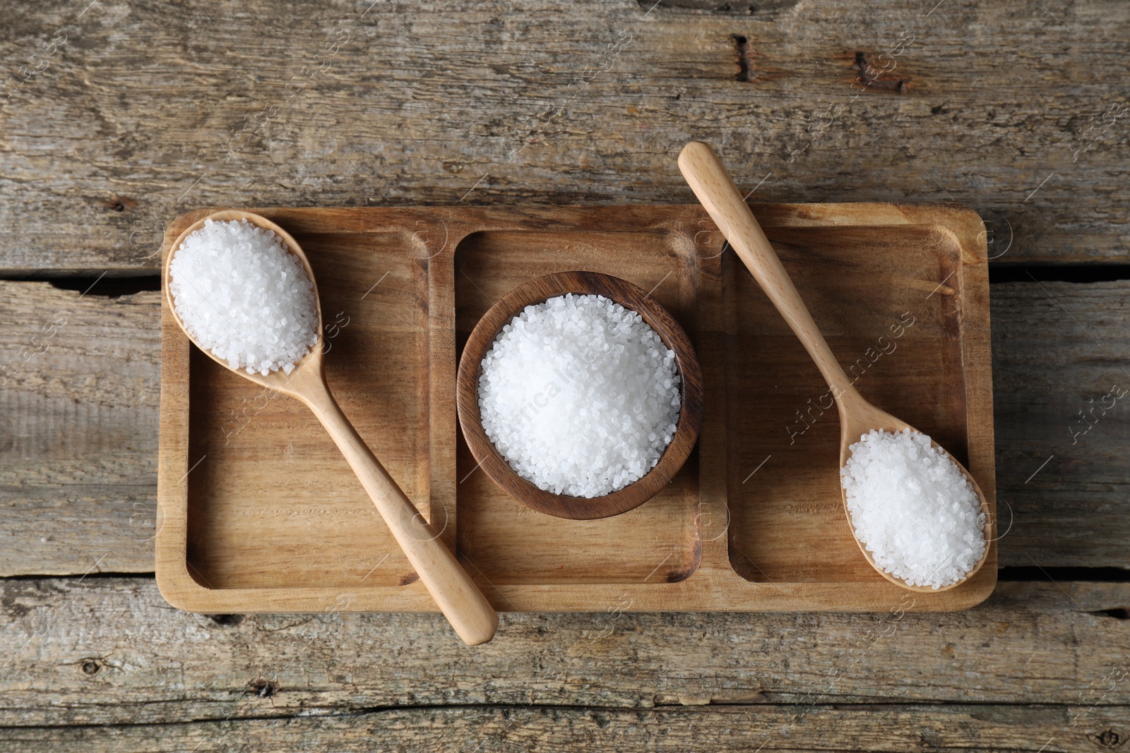 Photo of Organic salt in bowl and spoons on wooden table, top view