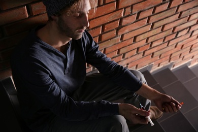 Photo of Male drug addict with syringe sitting on stairs near brick wall