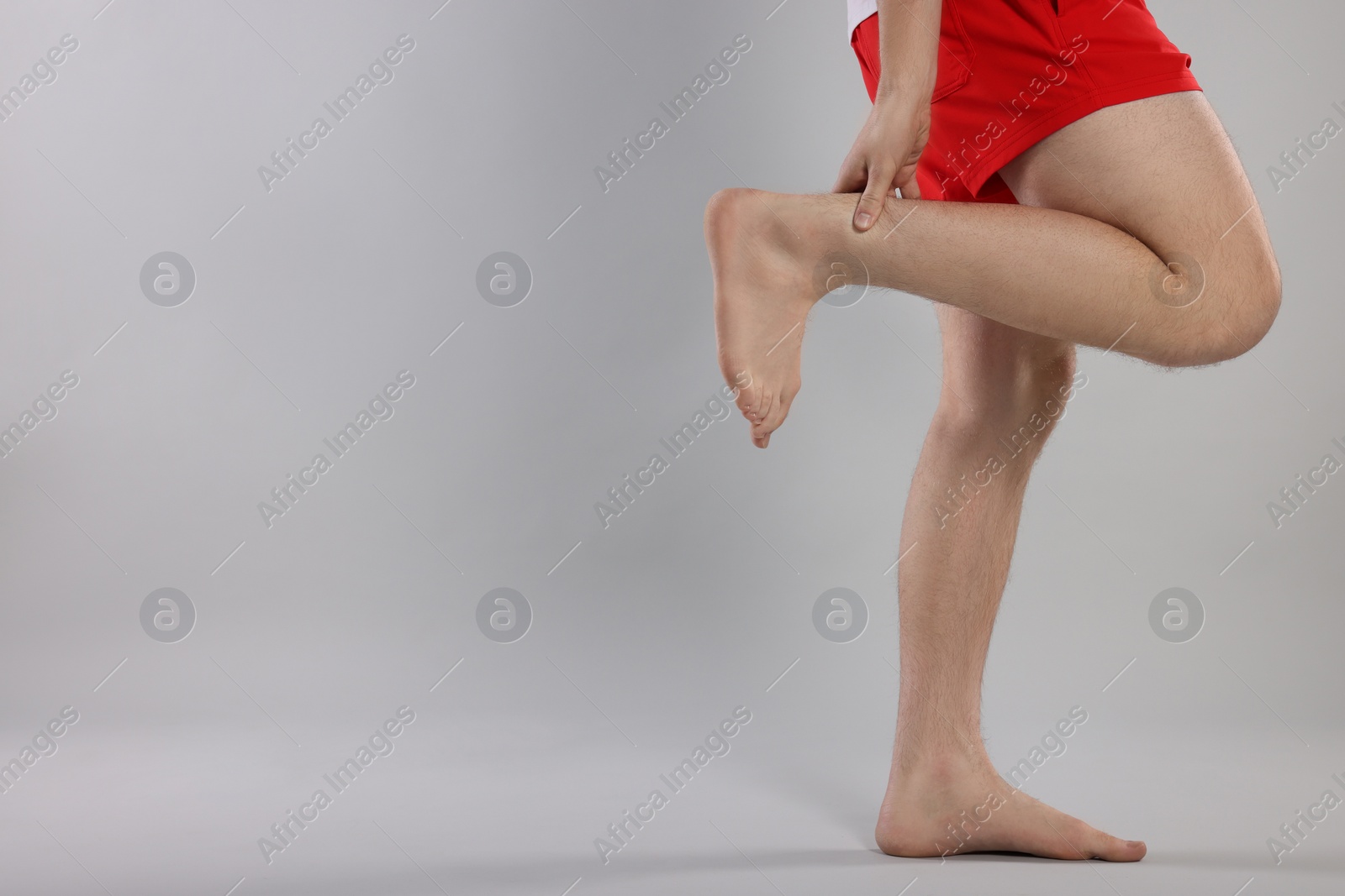 Photo of Man suffering from leg pain on grey background, closeup. Space for text