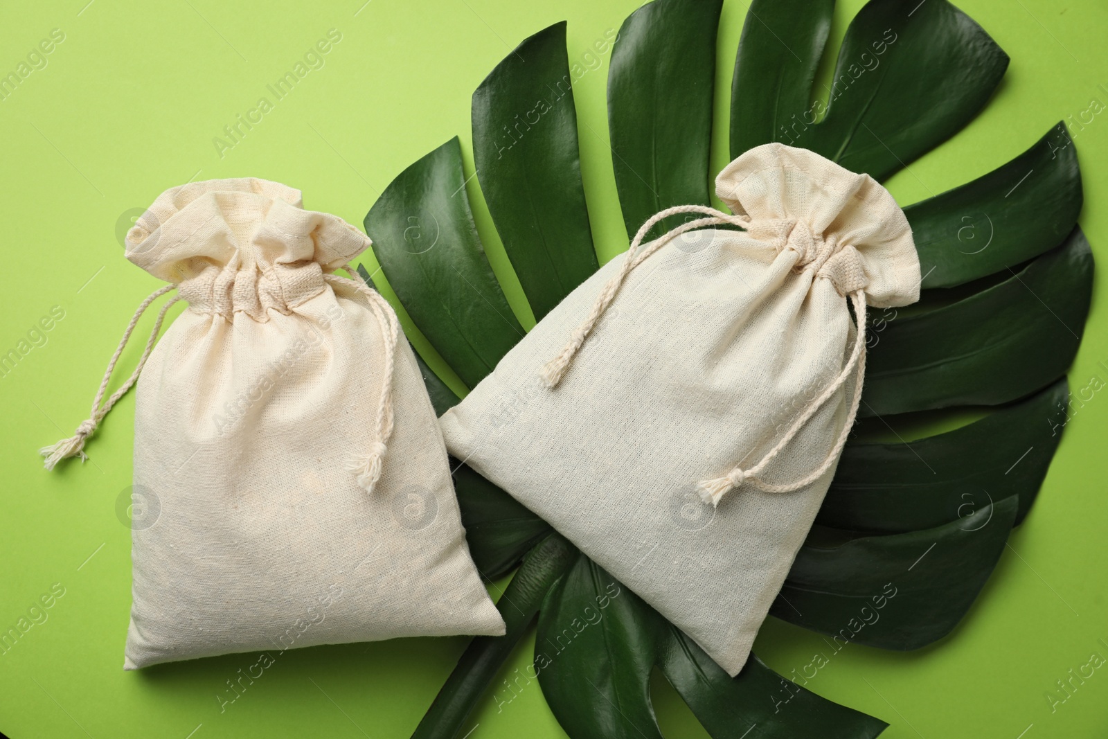 Photo of Cotton eco bags and monstera leaf on green background, flat lay