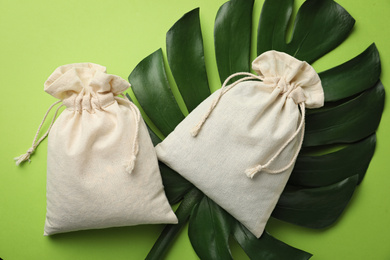 Photo of Cotton eco bags and monstera leaf on green background, flat lay
