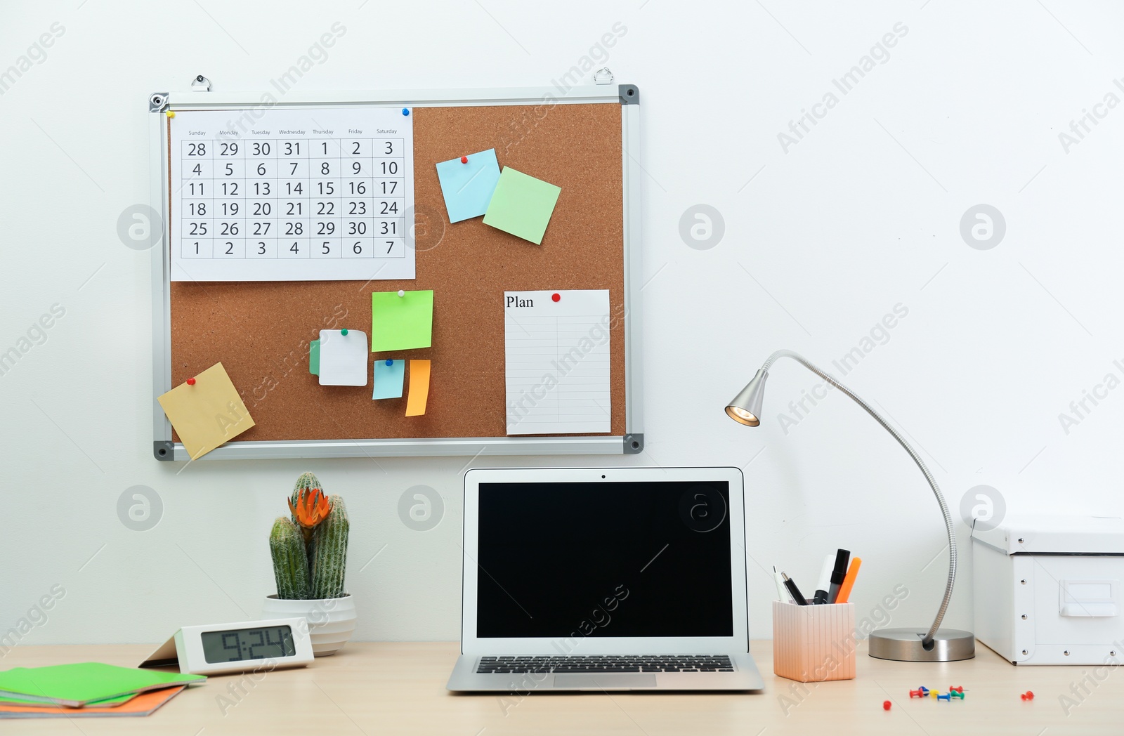 Photo of Workplace with cork board and laptop on table. Blank screen with space for text