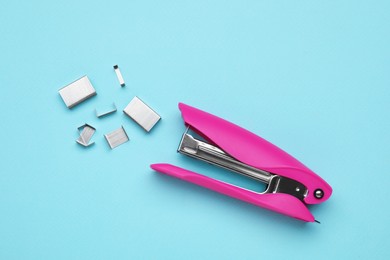Photo of New bright stapler with staples on light blue background, fat lay. School stationery