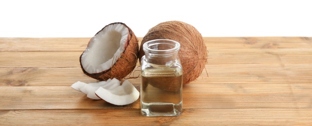 Photo of Ripe coconuts and jar with natural organic oil on wooden table against white background